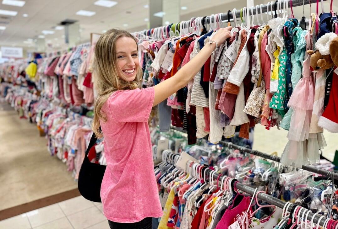 A mom and her child hug in between two rows of little girl clothes